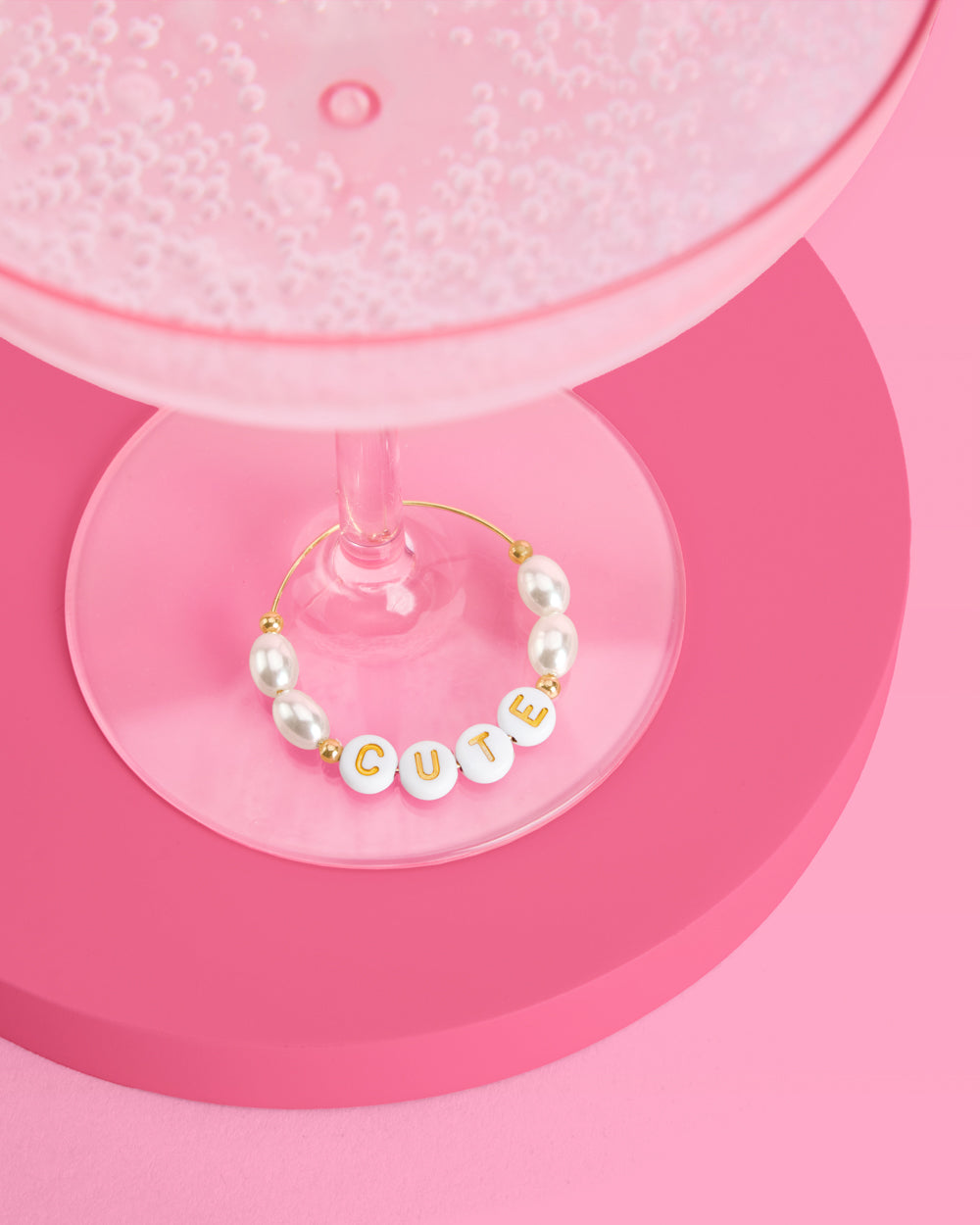 Pearl wine glass charm with 'CUTE' on a pink background