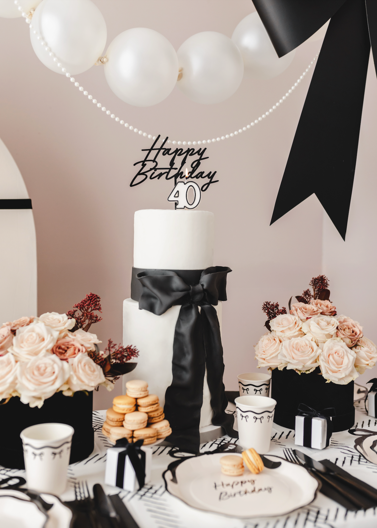 Birthday cake with black ribbon and 'Happy Birthday 40' topper, surrounded by floral arrangements and party decor.