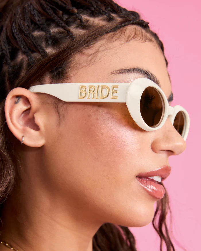Woman wearing white sunglasses with 'BRIDE' on a pink background