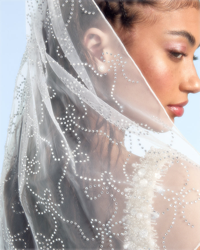 Close-up of a woman wearing a decorative veil against a clear blue sky.