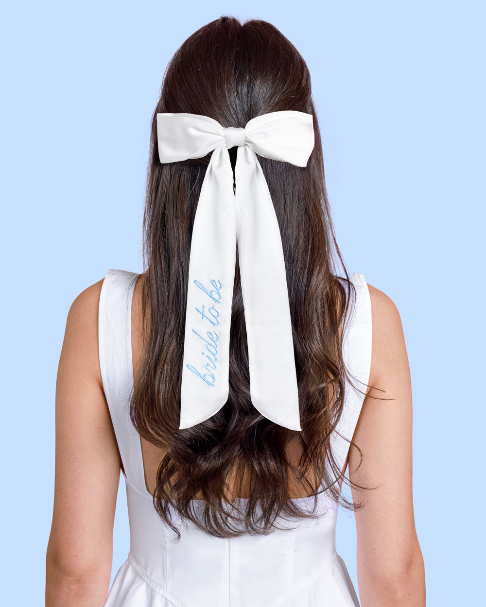 Woman with a white 'bride to be' bow in her hair against a light blue background