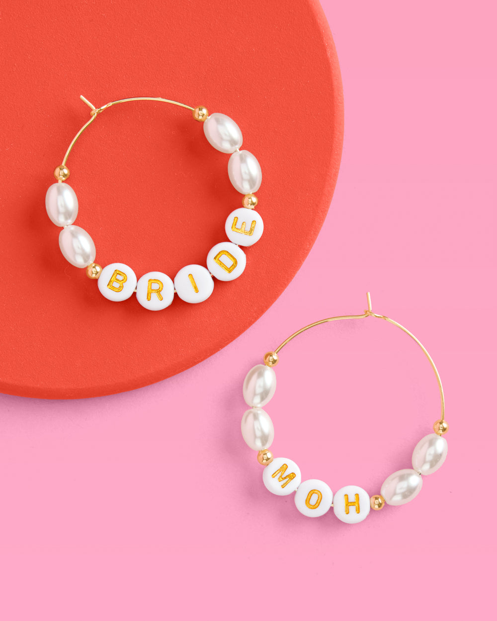 Pearl hoop earrings with 'BRIDE' and 'MOH' on a pink and red background
