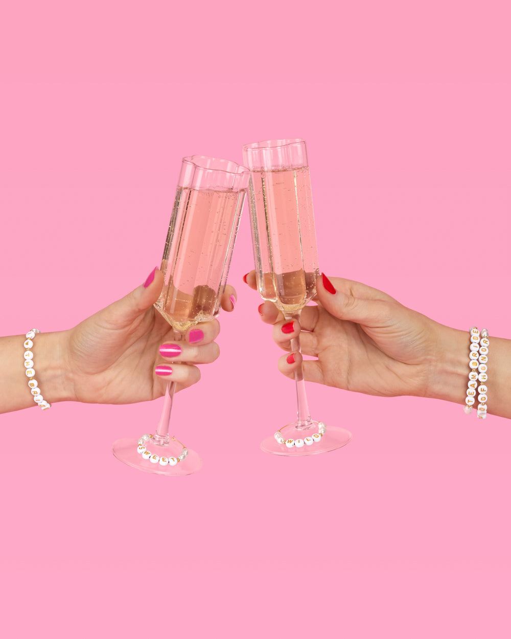 Two hands clinking champagne glasses against a pink background