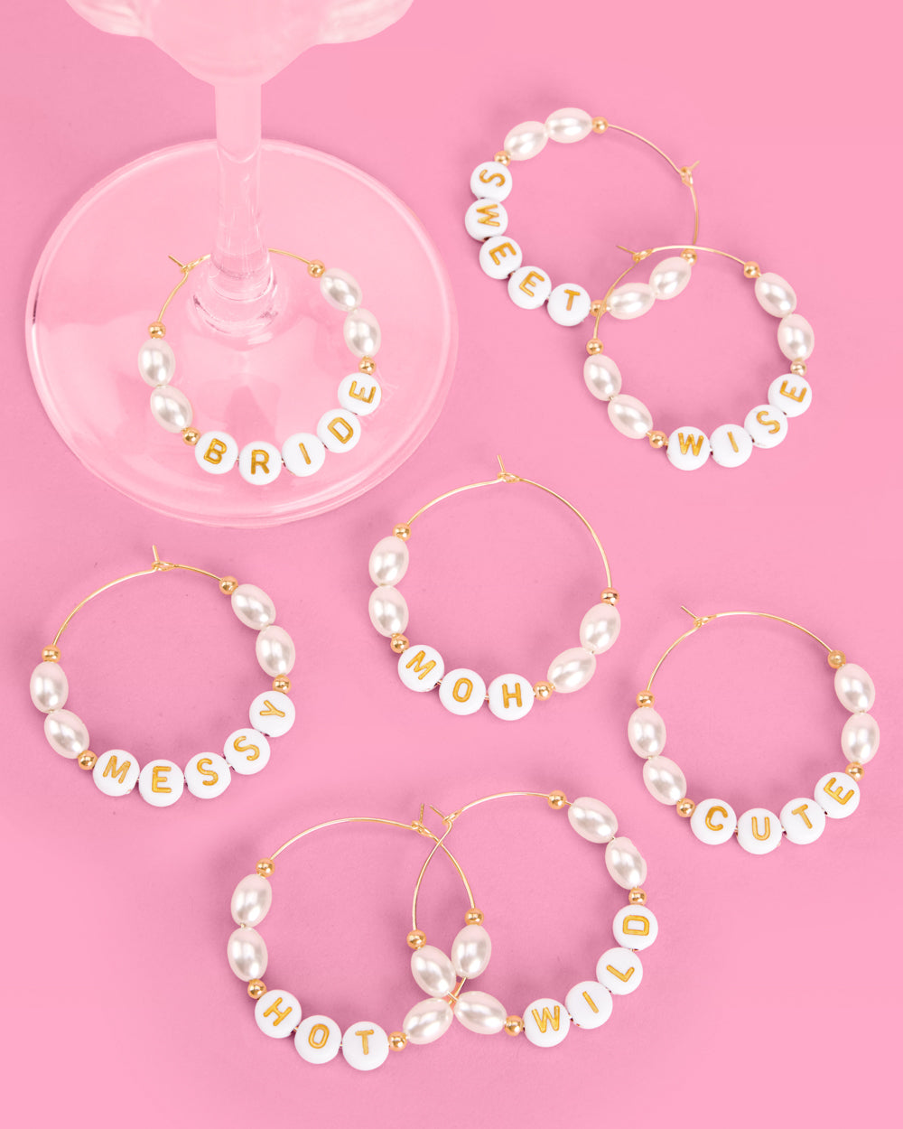 Set of pearl wine glass charms with various phrases on a pink background