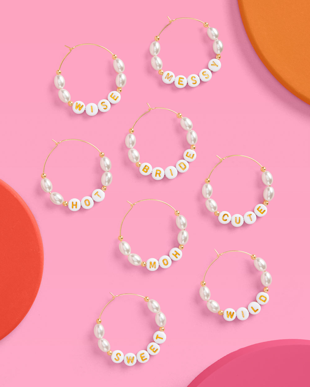 Set of pearl hoop earrings with word charms on a pink background