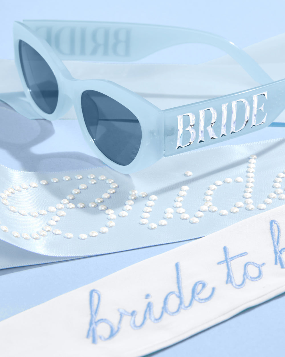 Blue sunglasses with 'BRIDE' and 'Bride to be' text on a light blue background