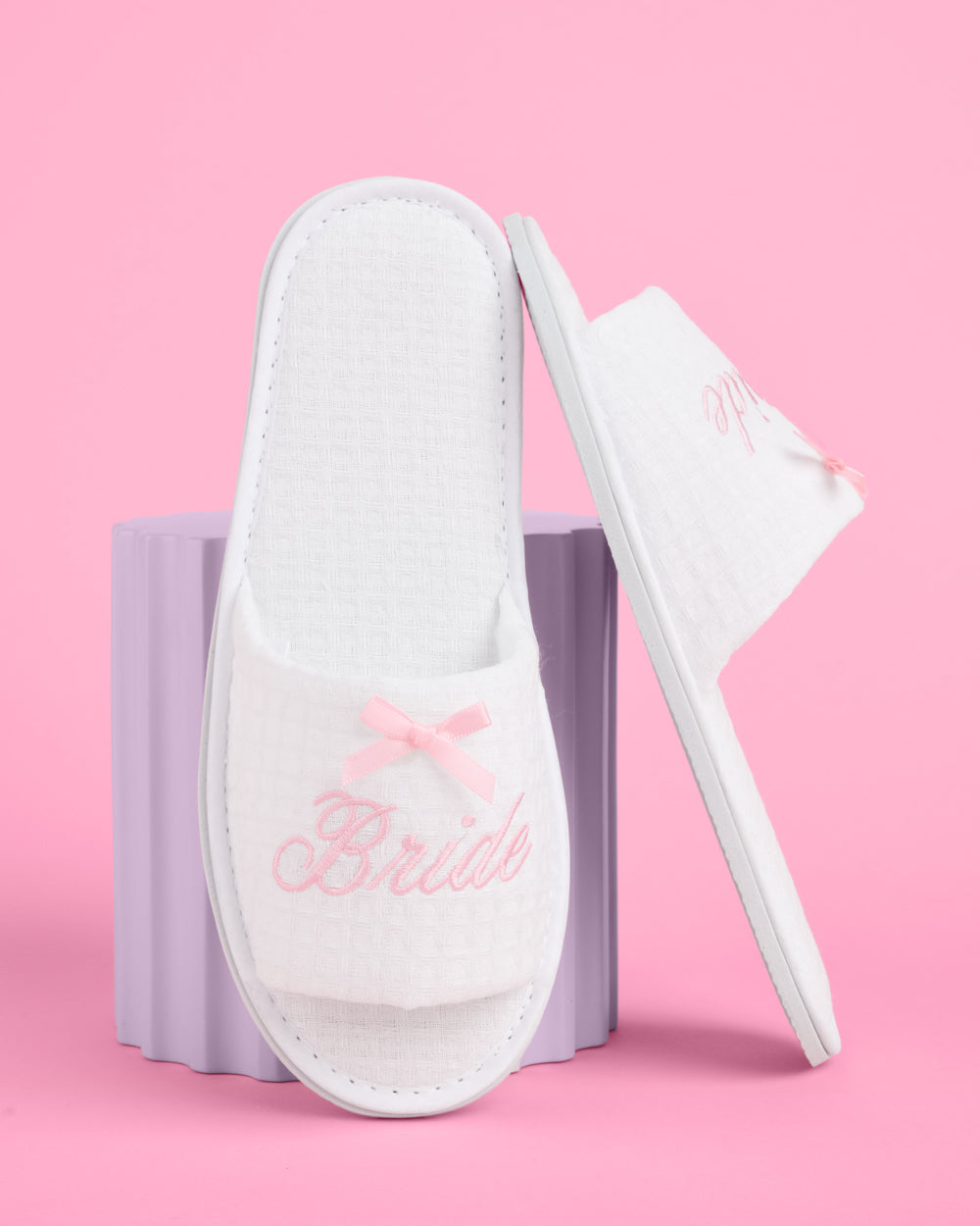 White slippers with 'Bride' text and pink bows on a pink background