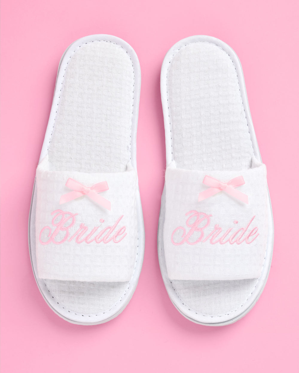 White slippers with 'Bride' text and pink bows on a pink background