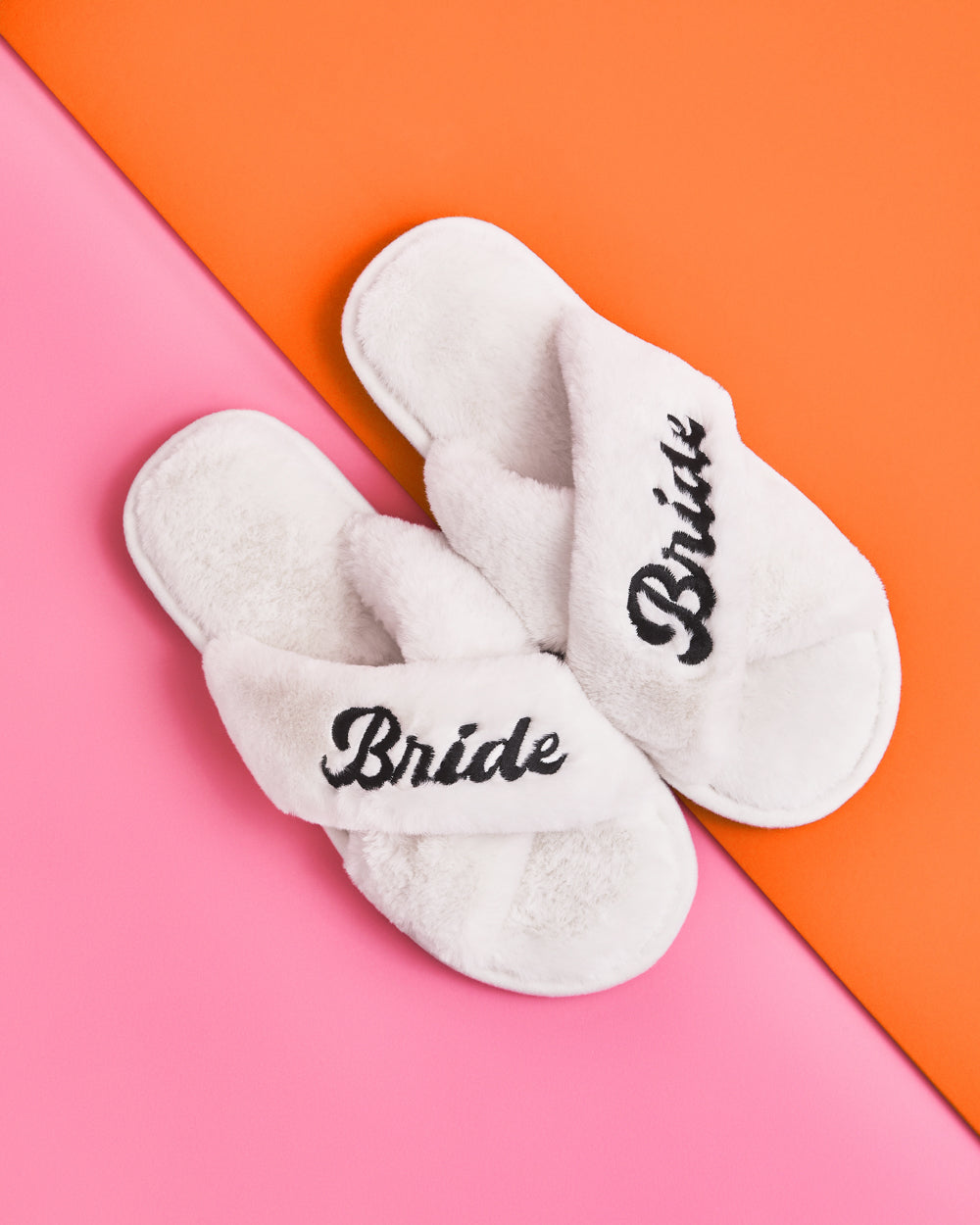 White slippers with &#39;Bride&#39; embroidery on a pink and orange background