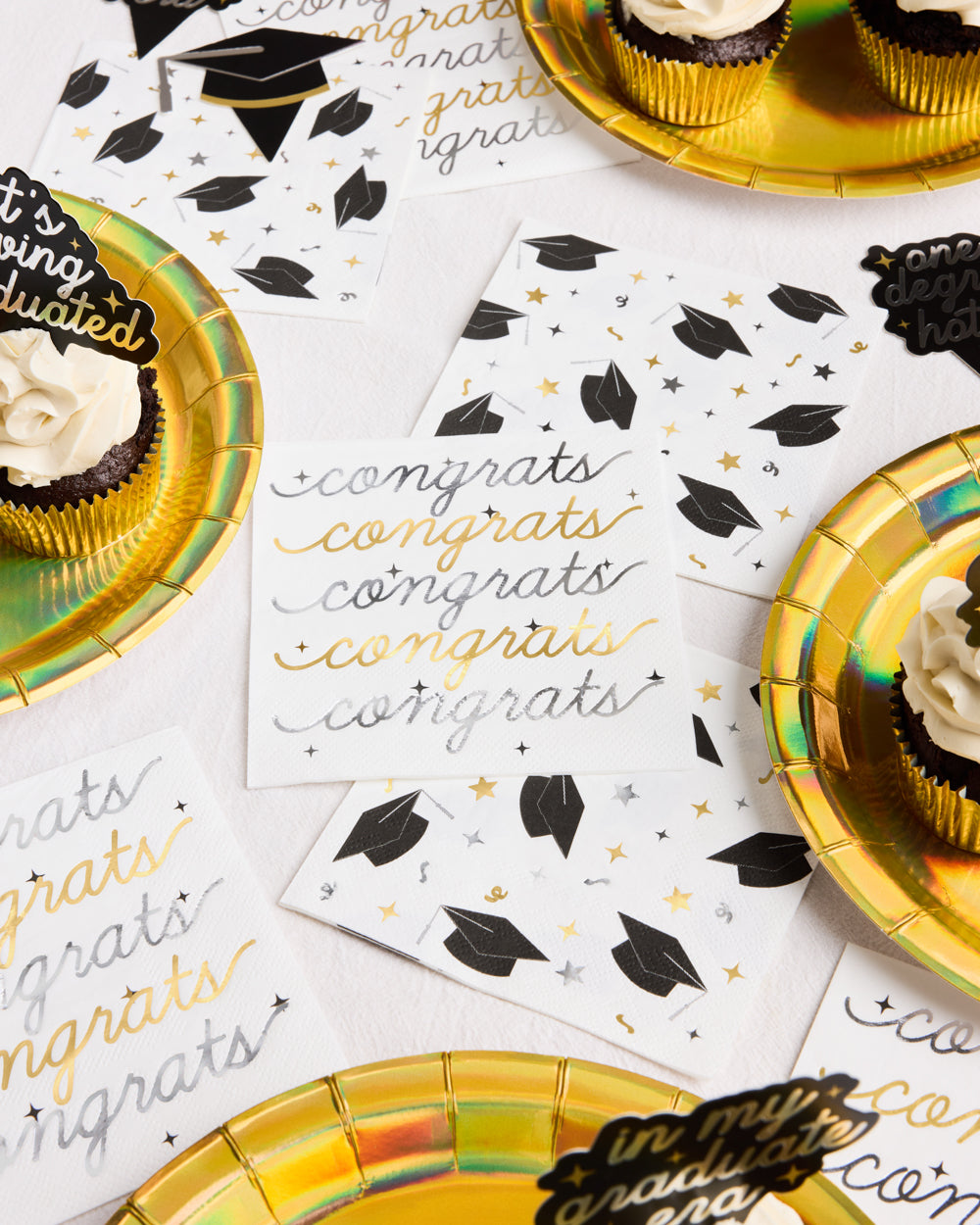 Graduation-themed party supplies including plates, napkins, and cupcakes on a white surface.
