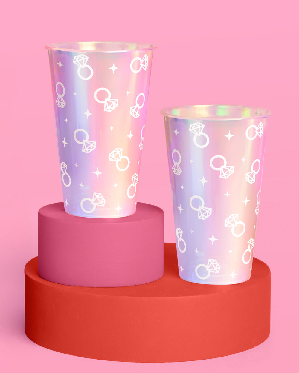 Two colorful cups with ring patterns on a pink and red platform against a pink background
