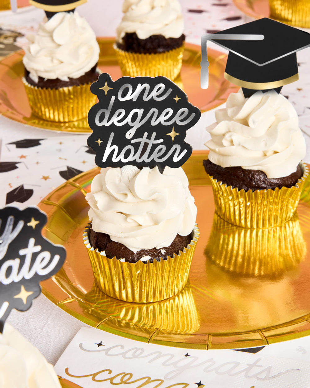 Cupcakes with gold wrappers and white frosting on a decorative plate with &#39;one degree hotter&#39; topper.