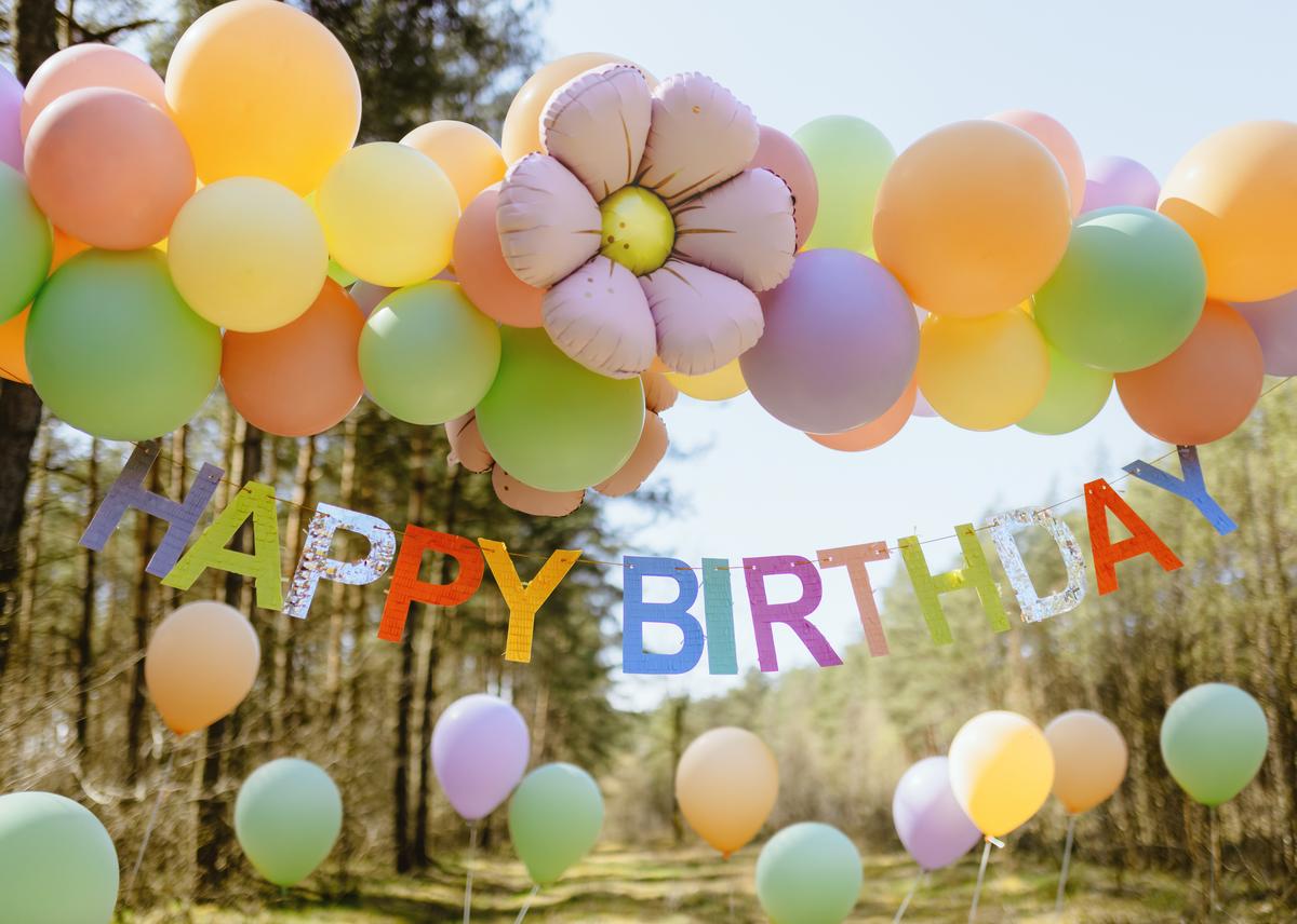 Colorful balloon arch with &#39;Happy Birthday&#39; banner in a forest setting