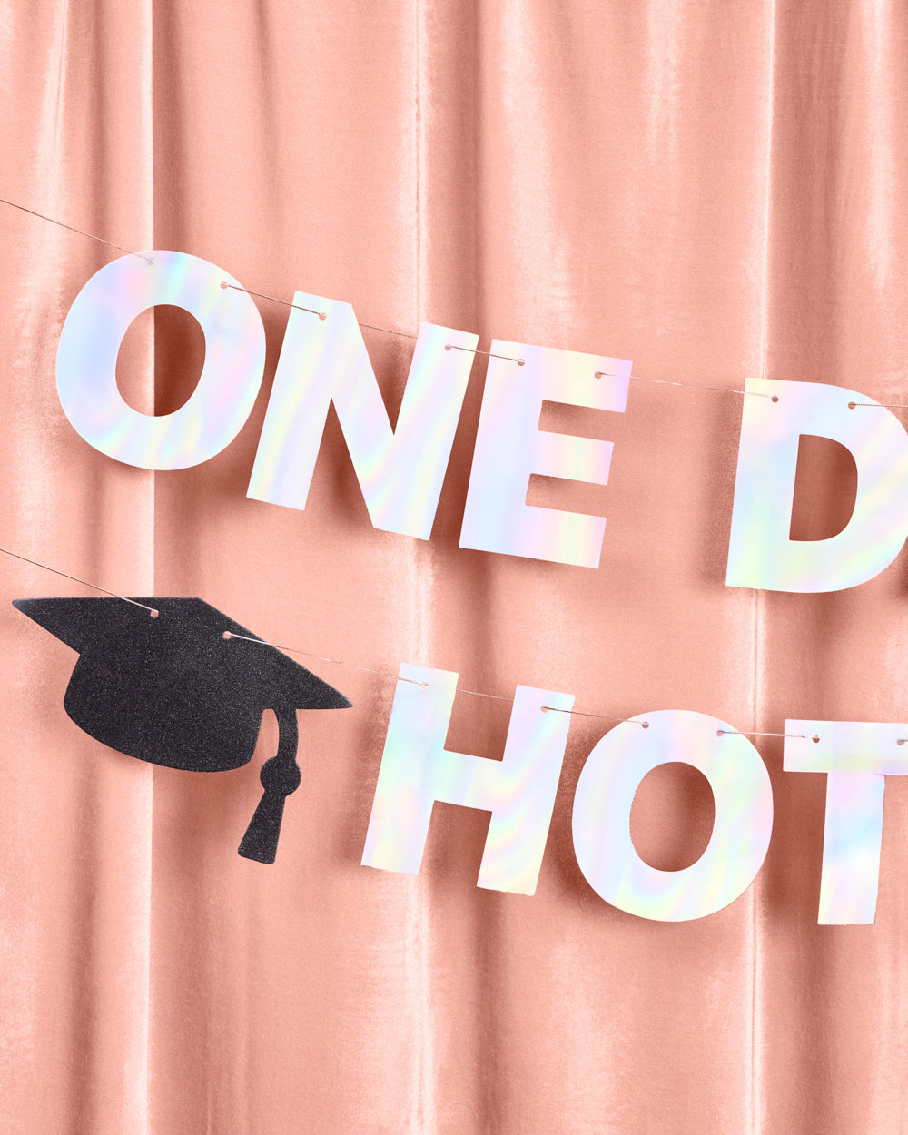 Holographic 'ONE DAY HOT' banner with a graduation cap on a pink curtain background
