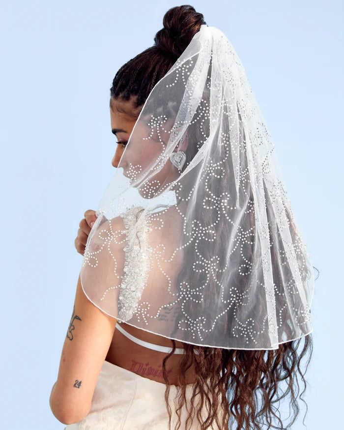Woman wearing a white veil with floral patterns against a clear blue sky