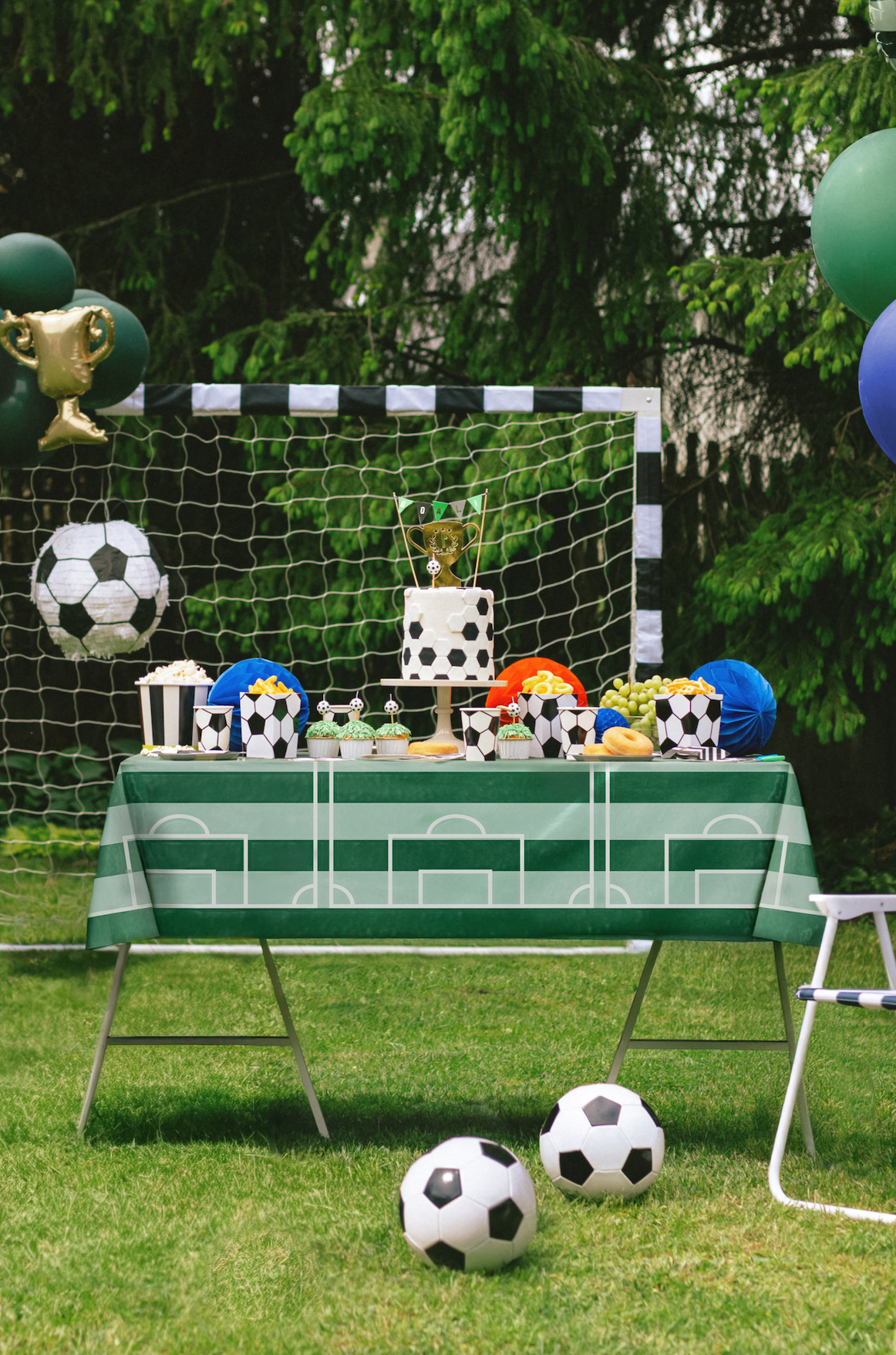 Soccer-themed party setup with table, balloons, and sports-themed decorations outdoors.
