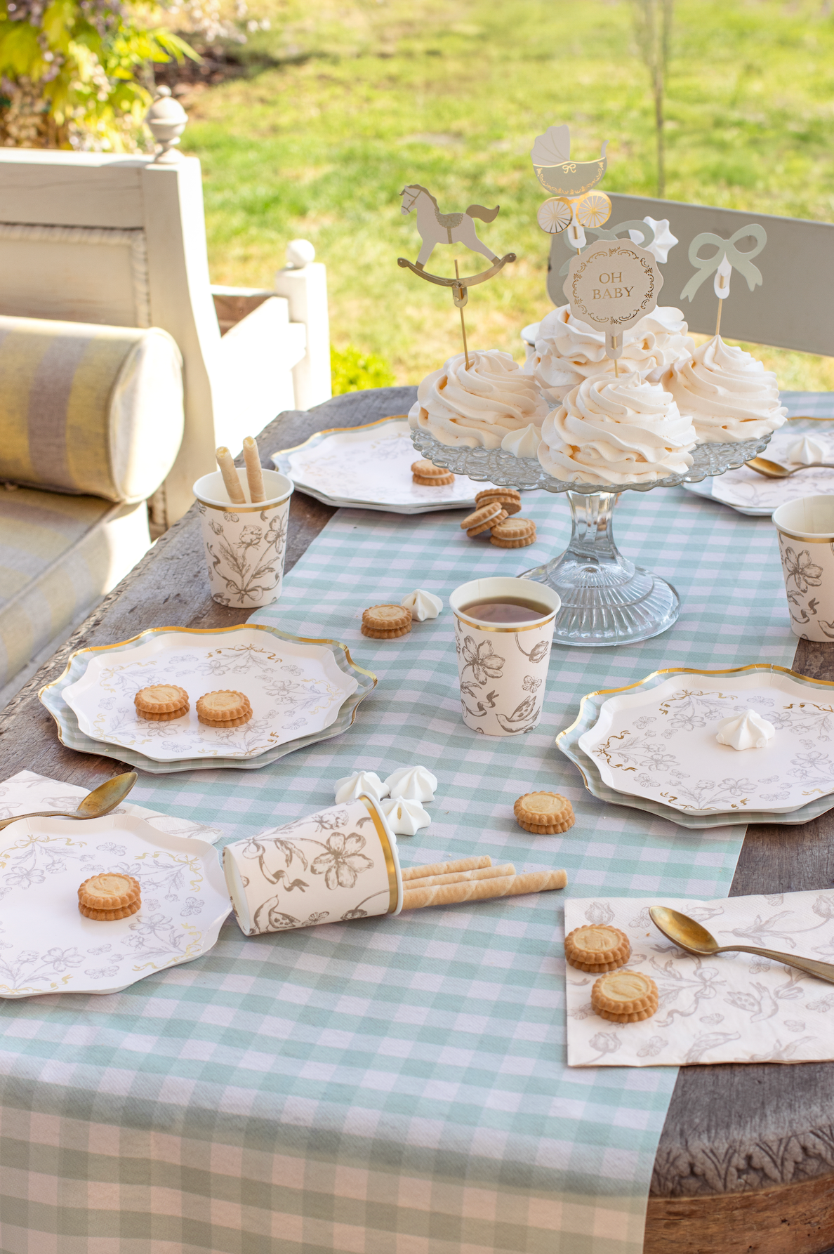 Table setting with cake, cookies, and coffee on a checkered tablecloth outdoors.