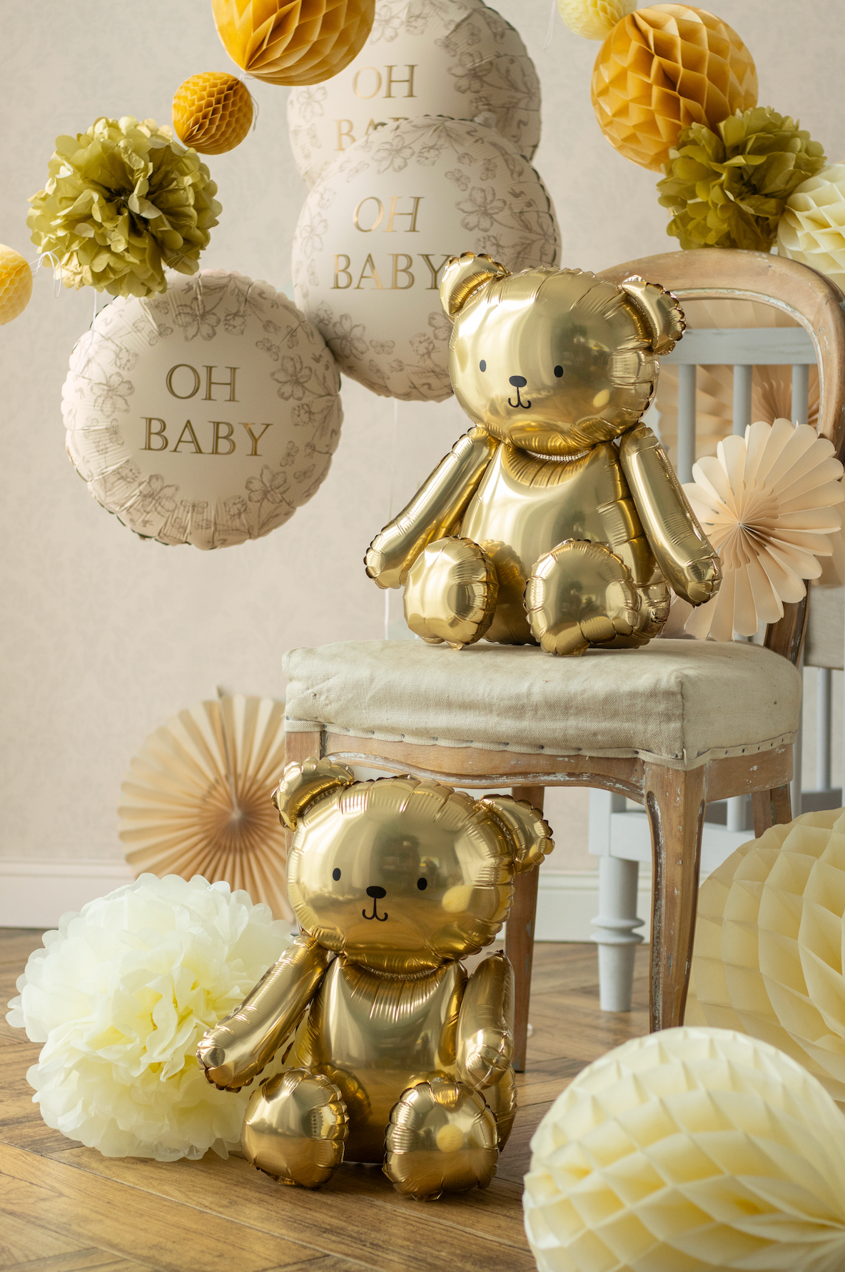 Gold teddy bears on a chair with decorative balloons and flowers in a baby shower setting.