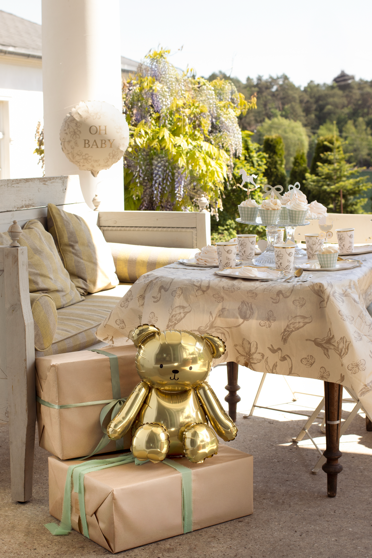 Gold teddy bear on wrapped presents with a table set outdoors