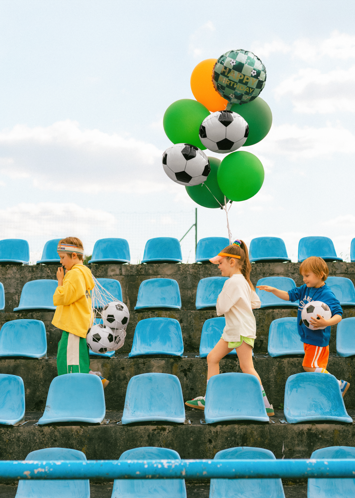 Children with soccer-themed balloons and jerseys in a stadium setting