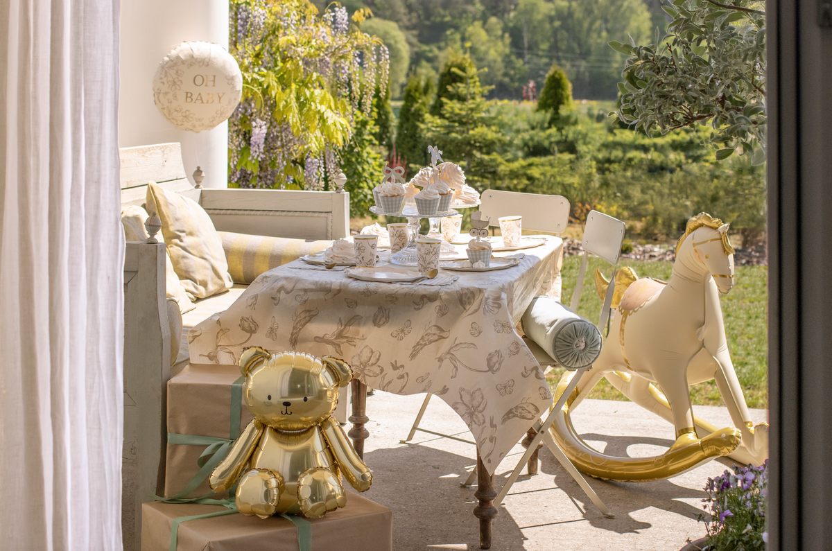 Decorative setting with a rocking horse, teddy bear, and table with teacups on a patio.
