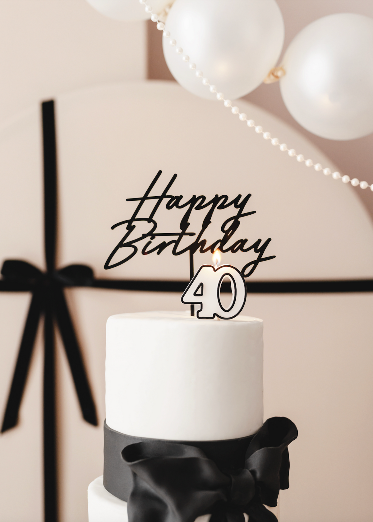 White cake with &#39;Happy Birthday 40&#39; topper against a neutral background