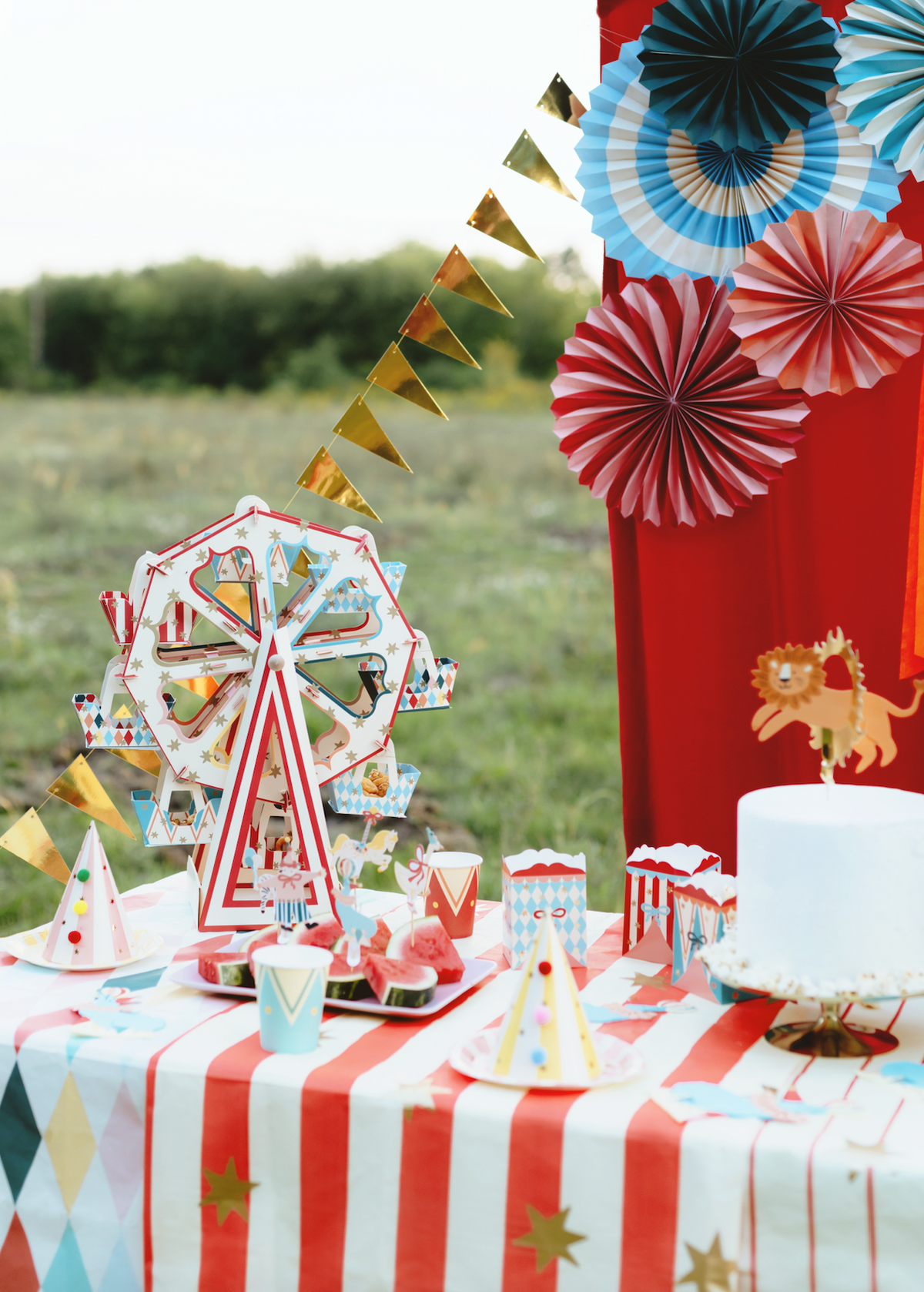 Carnival-themed table setting with a Ferris wheel, cake, and decorations outdoors.