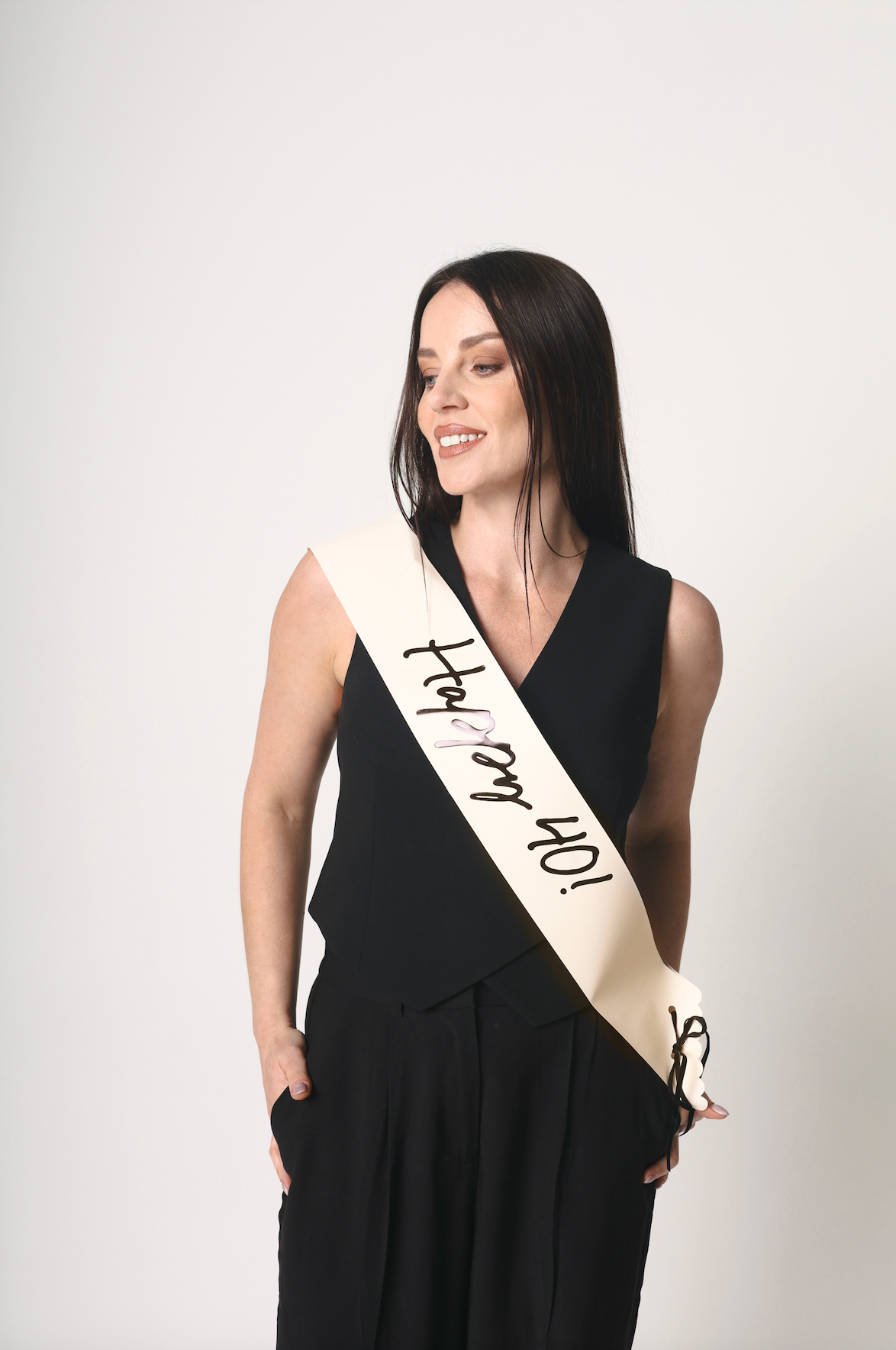 Woman wearing a sash with &#39;Happy 40!&#39; text on a plain background