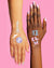 Two hands with colorful temporary tattoos on a pink background