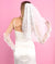 Person wearing a white dress and veil against a pink background