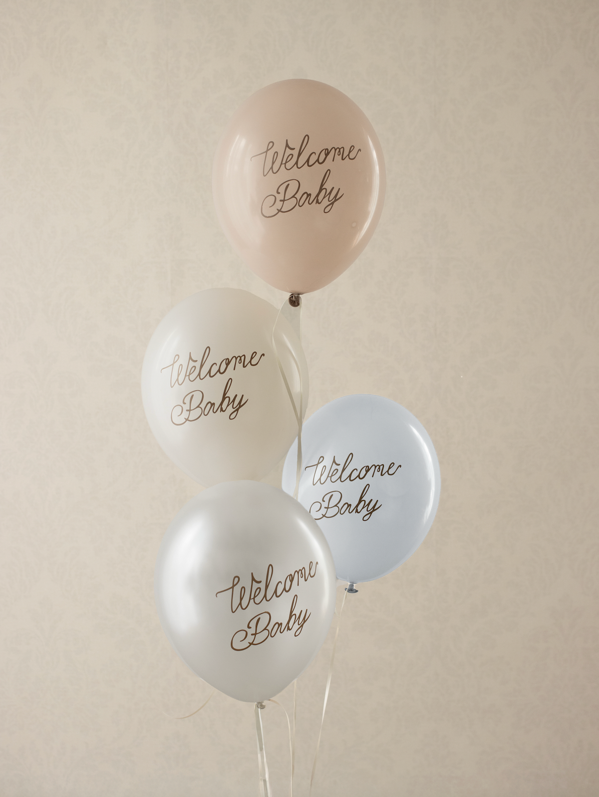 Four balloons with &#39;Welcome Baby&#39; text on a beige background