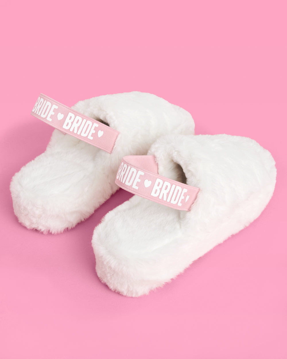 White fluffy slippers with 'Bride' straps on a pink background