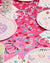 Colorful party supplies on a pink tablecloth with decorative elements.