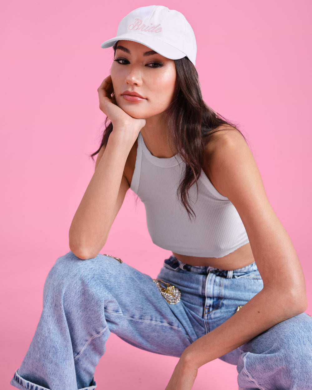 Woman wearing a white cap and light gray tank top against a pink background