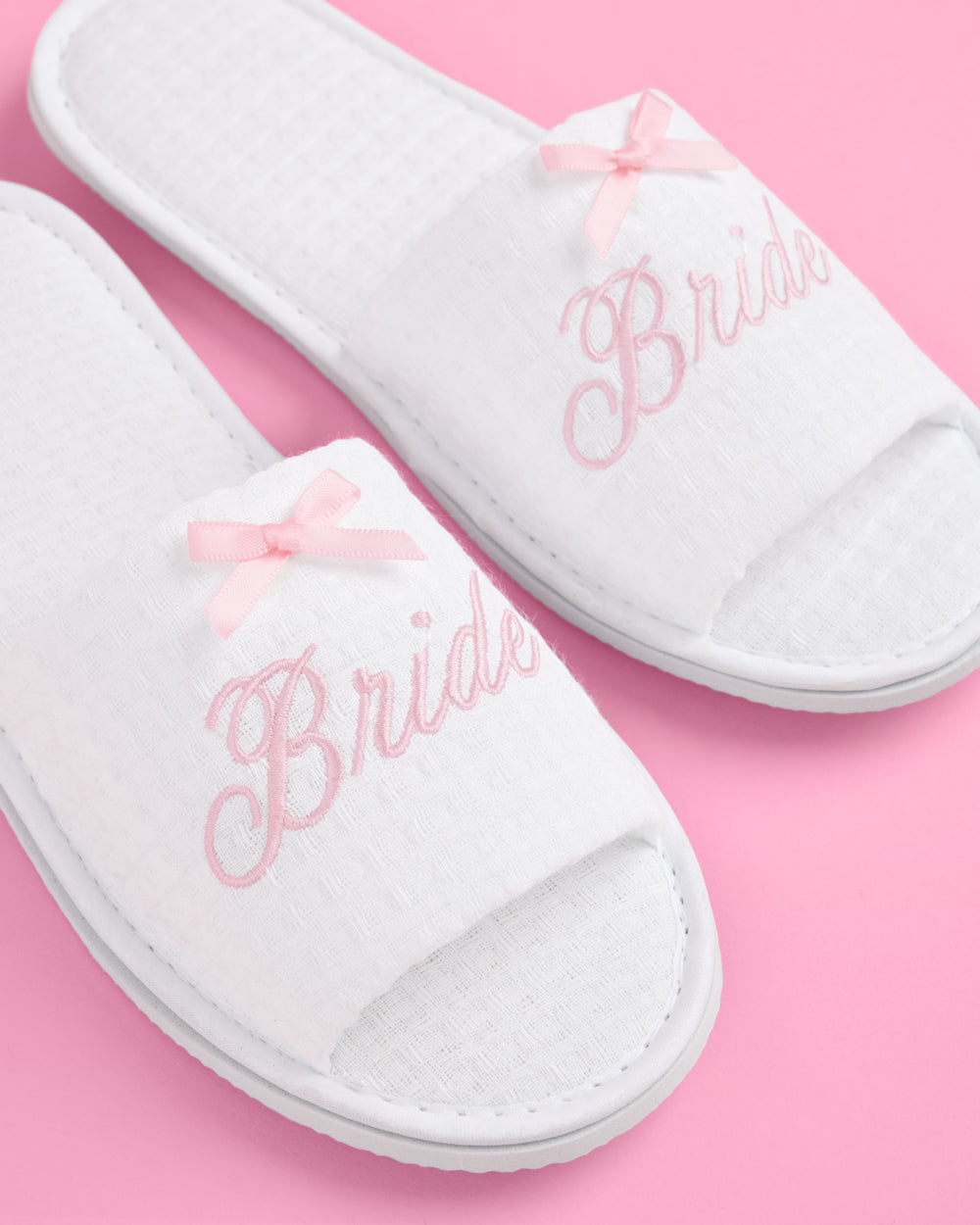 White slippers with &#39;Bride&#39; embroidery on a pink background